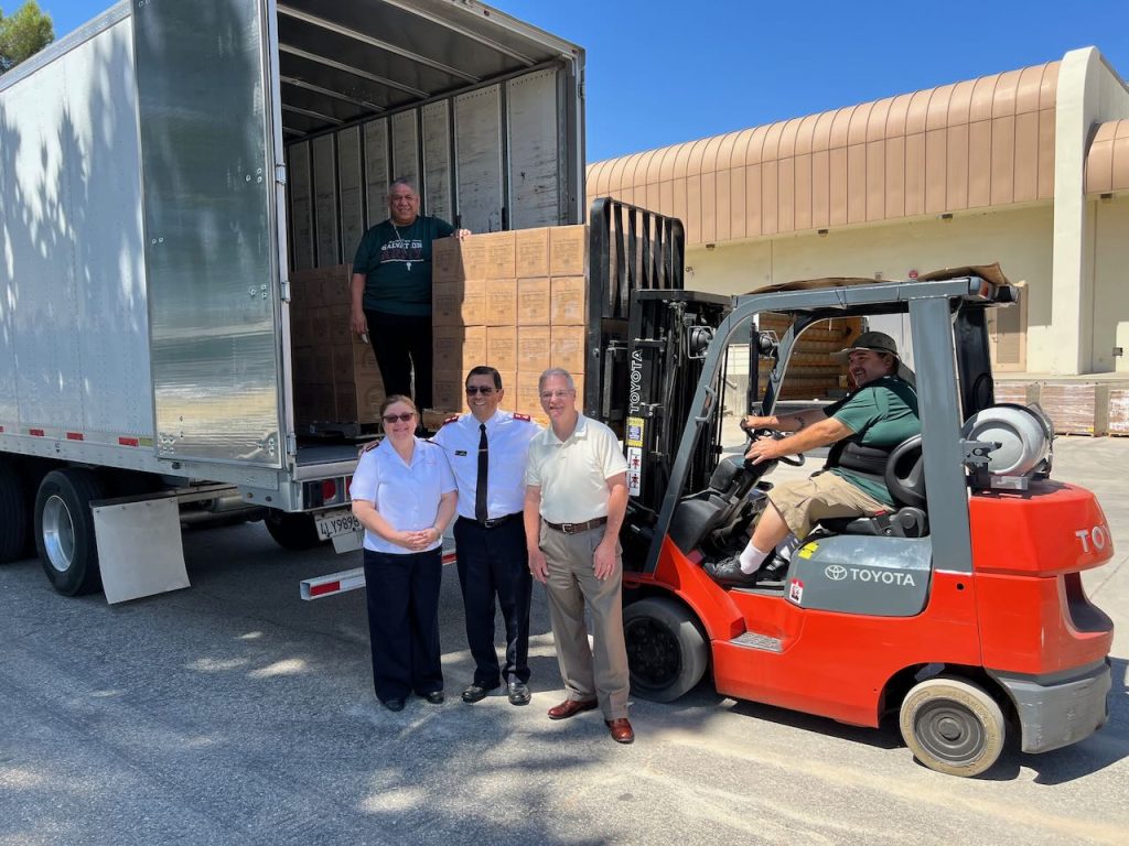 Photo caption: Salvation Army Major Adelma Braga, Major Isais Braga, The Church of Jesus Christ of the Latter-day Saints, Communications Director Lonnie Gallaher, Salvation Army officer Sam Valdez. In the truck Mike Delgado. In front of food donated by the church to serve the hungry in the San Bernardino area. 